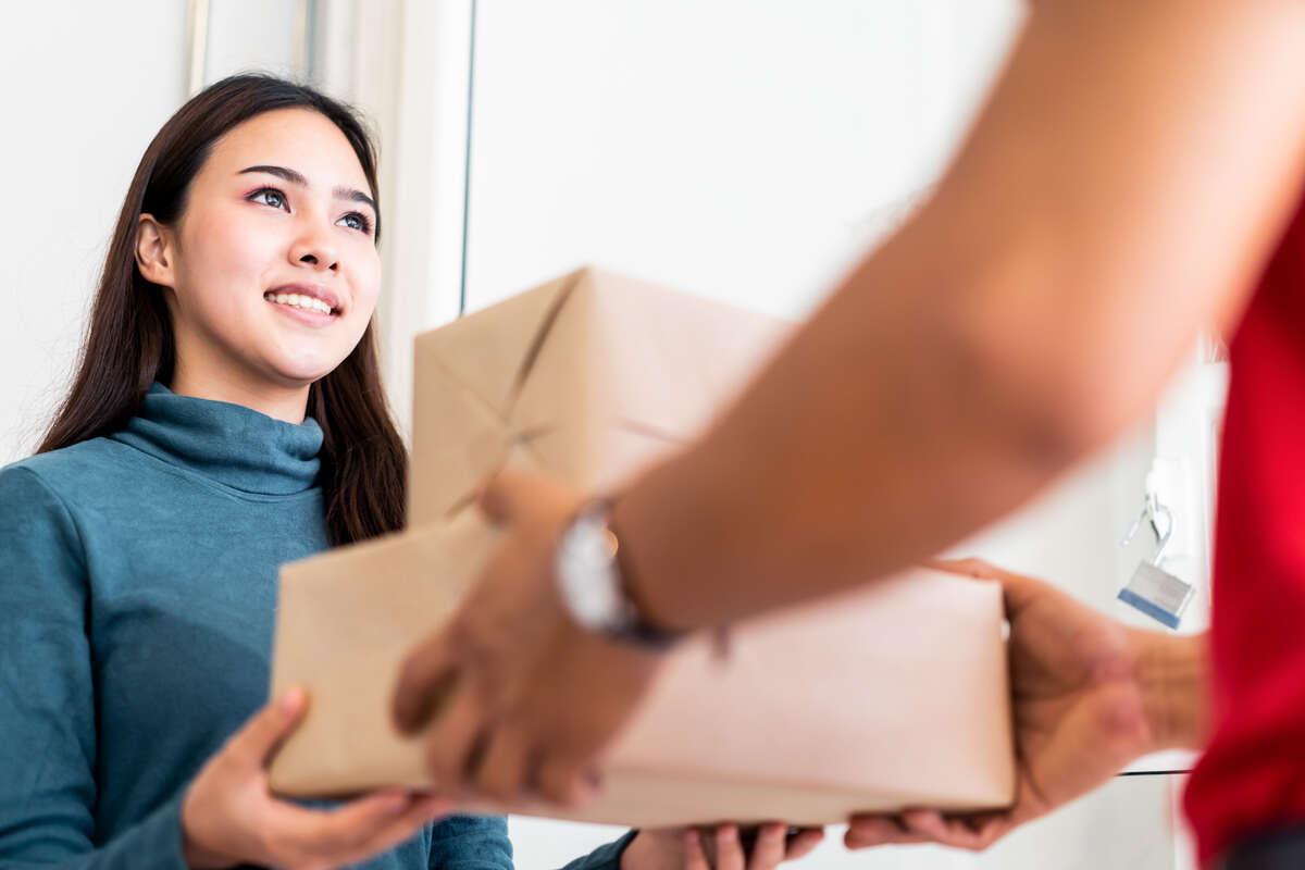 Woman in blue sweater smiles as she receives two packages from a person in red, conveying friendliness and satisfaction.