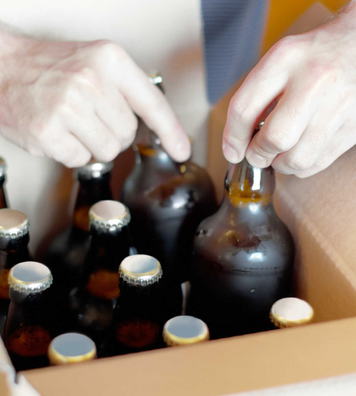 Hands placing capped beer bottles into a cardboard box.